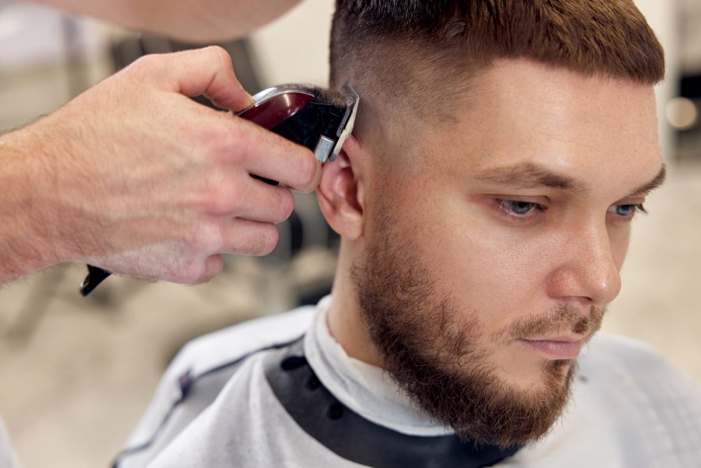 Barber trim hair with clipper on handsome bearded man