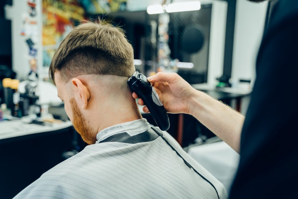 Male haircut with electric razor. Barber makes haircut for client at the barber shop by using